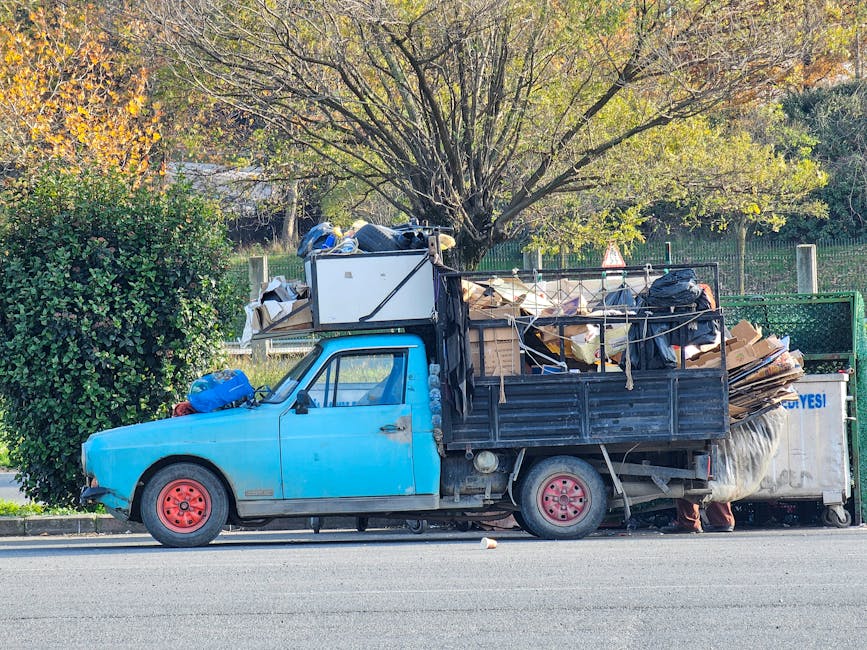 The image depicts an outdoor scene of a driveway or storage area with a large collection of waste and recyclable materials. In the foreground, there are several green and red plastic wheelie bins with