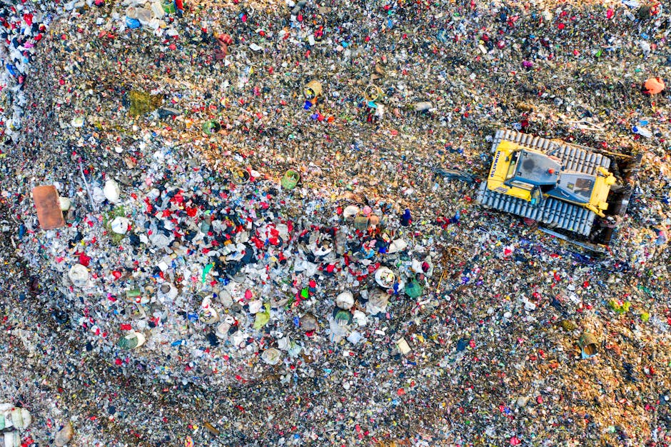 A close-up view of a heap of crushed aluminum soft drink cans and crushed plastic beverage bottles, mostly in silver, red, blue, black, and gold colors. The cans are aluminum with smooth, reflective s
